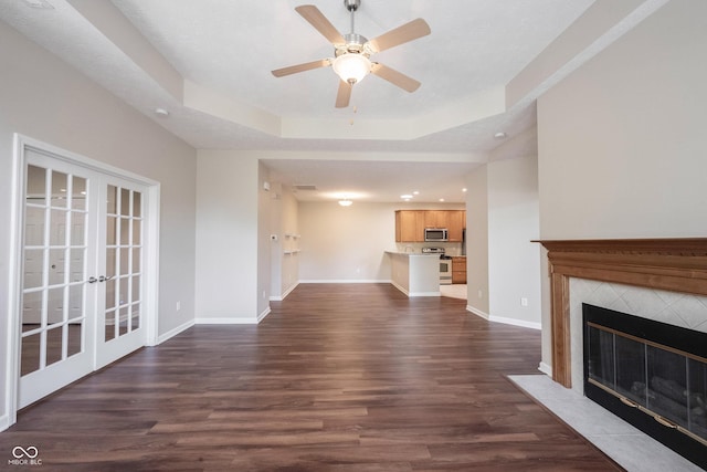 6586 Quail Run, Fishers, IN 46038 - unfurnished living room featuring dark wood-type flooring, a ceiling fan, a tiled fireplace, a tray ceiling, and french doors