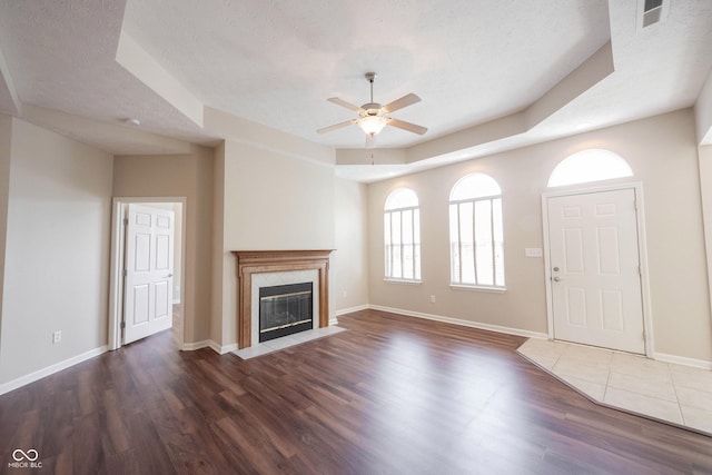 6586 Quail Run, Fishers, IN 46038 - unfurnished living room with a ceiling fan, dark wood-style flooring, a tiled fireplace, a textured ceiling, and a tray ceiling