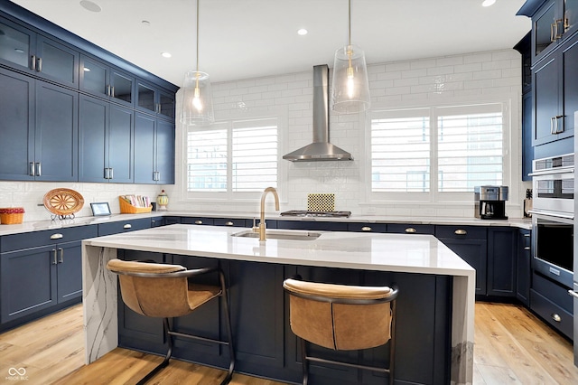 906 Berkhamsted Ln, Carmel, IN 46032 - kitchen with wall chimney exhaust hood, tasteful backsplash, a breakfast bar area, light wood-style flooring, and stainless steel double oven