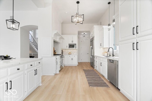 12208 Island Dr, Indianapolis, IN 46256 - kitchen with built in appliances, white cabinetry, light wood-type flooring, tasteful backsplash, and a chandelier