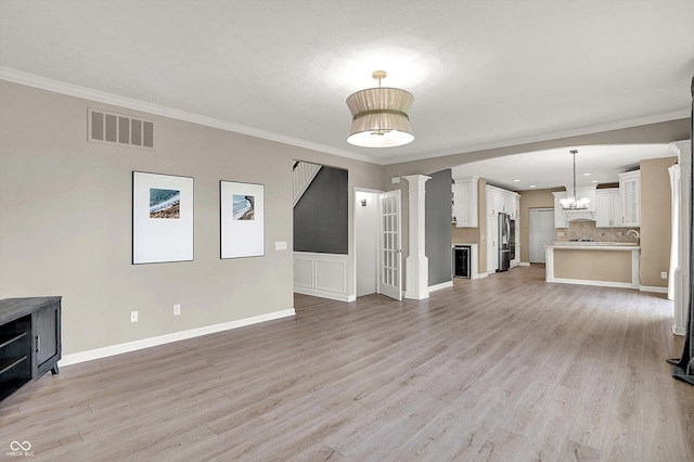 3345 Kilkenny Cir, Carmel, IN 46032 - unfurnished living room featuring ornate columns, ornamental molding, light wood finished floors, and a chandelier