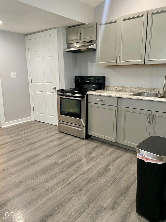 3464 N Bancroft St, Indianapolis, IN 46218 - kitchen with stainless steel range with electric stovetop, gray cabinets, under cabinet range hood, light wood-style floors, and light countertops