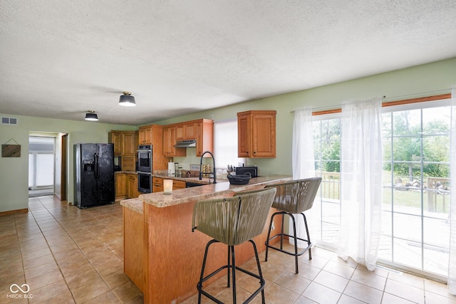 13041 S Finer St, Pimento, IN 47866 - kitchen featuring black refrigerator with ice dispenser, a textured ceiling, under cabinet range hood, brown cabinets, and light tile patterned flooring