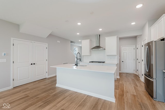 9751 Behner Dr, Fishers, IN 46250 - kitchen featuring wall chimney exhaust hood, freestanding refrigerator, light wood-style flooring, gas stovetop, and an island with sink