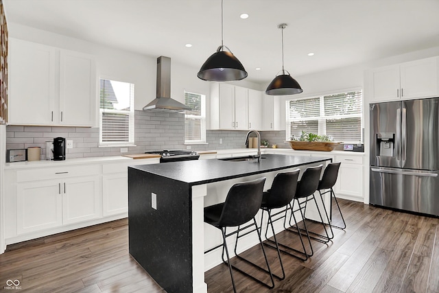 2720 Guilford Ave, Indianapolis, IN 46205 - kitchen with stainless steel refrigerator with ice dispenser, wall chimney range hood, tasteful backsplash, an island with sink, and wood finished floors