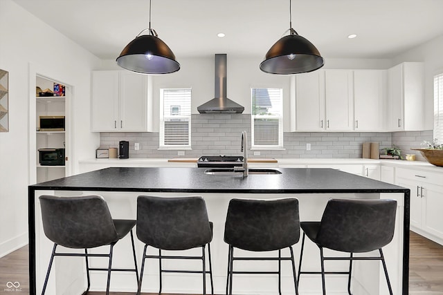 2720 Guilford Ave, Indianapolis, IN 46205 - kitchen with wall chimney exhaust hood, stainless steel microwave, decorative backsplash, white cabinetry, and a kitchen bar