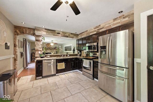 9265 Brunson Run, Indianapolis, IN 46256 - kitchen featuring stainless steel appliances, ceiling fan, dark brown cabinetry, arched walkways, and light tile patterned floors