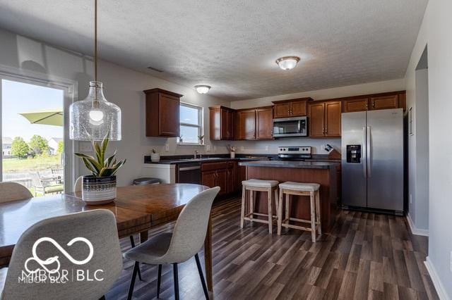 12584 Cold Stream Rd, Noblesville, IN 46060 - kitchen with appliances with stainless steel finishes, dark countertops, dark wood-type flooring, a center island, and a textured ceiling