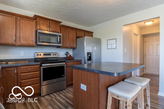 12584 Cold Stream Rd, Noblesville, IN 46060 - kitchen with appliances with stainless steel finishes, dark countertops, dark wood-type flooring, a breakfast bar area, and a textured ceiling