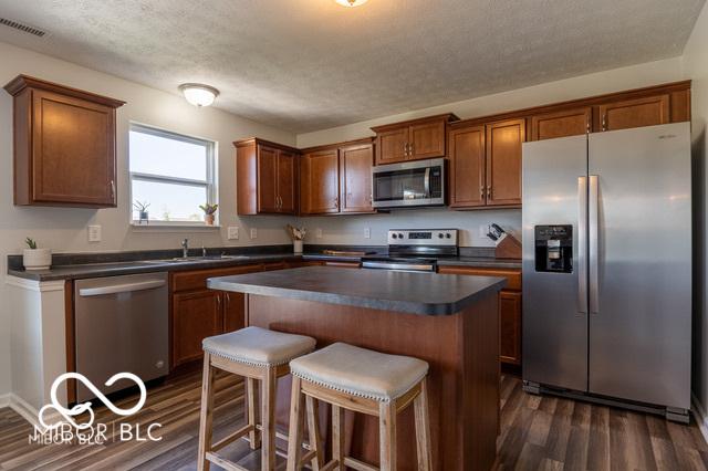 12584 Cold Stream Rd, Noblesville, IN 46060 - kitchen featuring stainless steel appliances, dark countertops, dark wood-style floors, a center island, and a textured ceiling