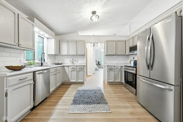 5982 Oak Hill E Dr, Plainfield, IN 46168 - kitchen featuring stainless steel appliances, vaulted ceiling, a textured ceiling, decorative backsplash, and light wood-style floors