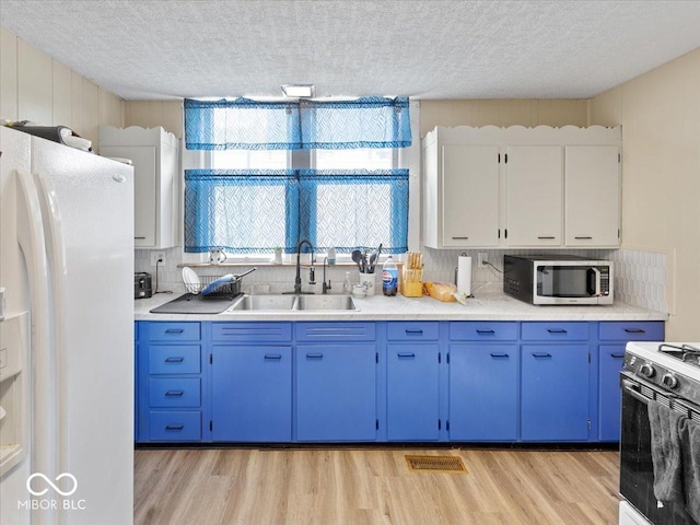 215 N E St, Greensburg, IN 47240 - kitchen featuring white refrigerator with ice dispenser, stainless steel microwave, range with electric stovetop, blue cabinetry, and light wood-style floors