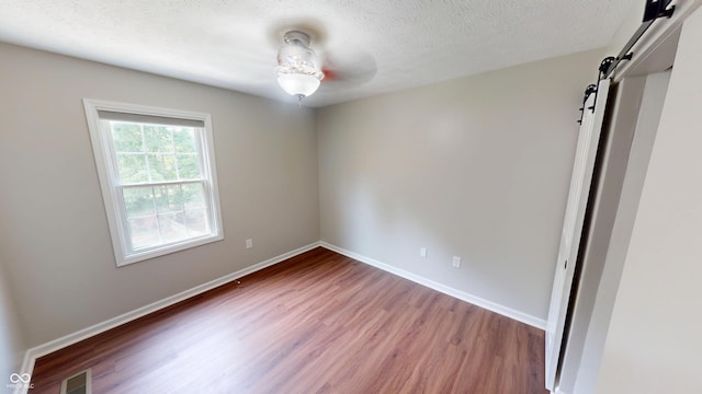 9831 Deering St, Fishers, IN 46037 - empty room with wood finished floors, a barn door, a textured ceiling, and a ceiling fan