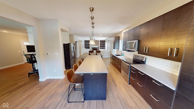 9831 Deering St, Fishers, IN 46037 - kitchen with stainless steel appliances, a breakfast bar area, decorative backsplash, light countertops, and light wood-type flooring