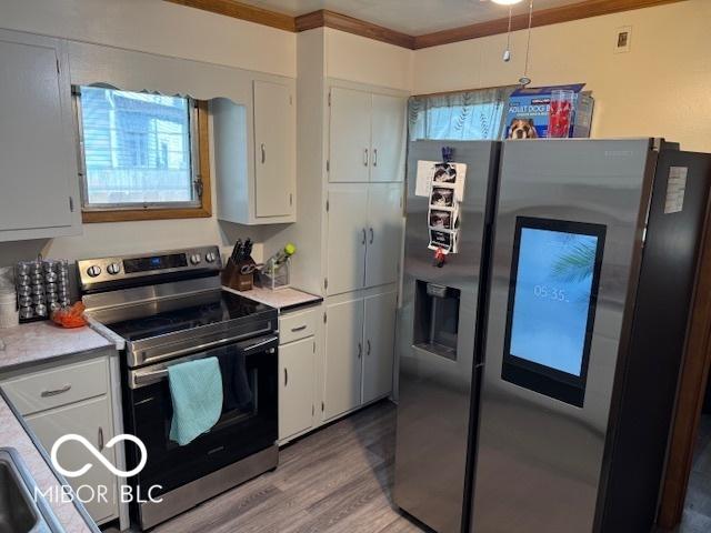 2830 Guilford Ave, Indianapolis, IN 46205 - kitchen featuring stainless steel appliances, white cabinets, light countertops, light wood-type flooring, and crown molding