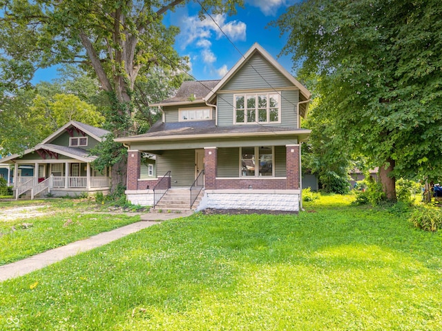 5511 E University Ave, Indianapolis, IN 46219 - view of front of house featuring covered porch, brick siding, a front lawn, and roof with shingles