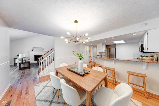 8178 Foxchase Cir, Indianapolis, IN 46256 - dining room featuring a chandelier, a fireplace with raised hearth, light wood-type flooring, a textured ceiling, and stairs