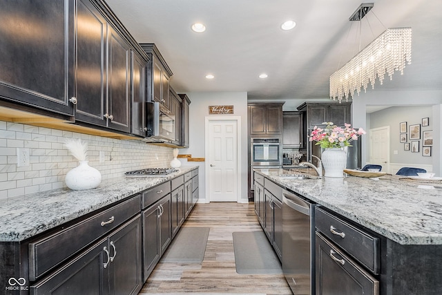 12634 Mustard Seed Ct, Fishers, IN 46038 - kitchen with appliances with stainless steel finishes, light wood-style flooring, light stone countertops, decorative backsplash, and a kitchen island with sink