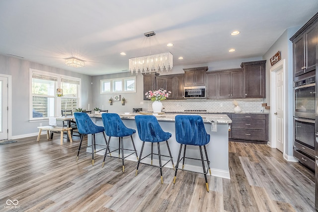 12634 Mustard Seed Ct, Fishers, IN 46038 - kitchen featuring stainless steel appliances, dark brown cabinets, light wood-style flooring, a kitchen breakfast bar, and decorative backsplash