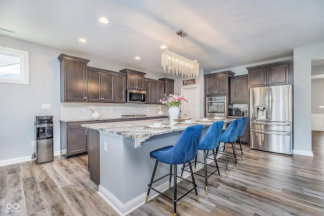 12634 Mustard Seed Ct, Fishers, IN 46038 - kitchen featuring stainless steel appliances, dark brown cabinetry, a chandelier, light stone counters, and tasteful backsplash