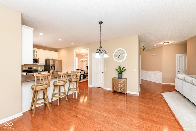 13700 Stanford Dr, Carmel, IN 46074 - kitchen with stainless steel appliances, a kitchen breakfast bar, a chandelier, light wood-type flooring, and glass insert cabinets
