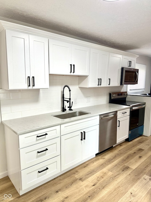 405 E Cowing Dr, Muncie, IN 47303 - kitchen with stainless steel appliances, white cabinets, a textured ceiling, light wood-style flooring, and tasteful backsplash