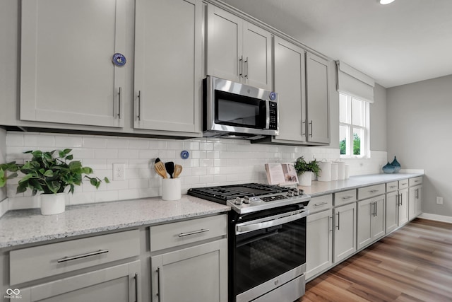 5343 Pelion Pl, Mccordsville, IN 46055 - kitchen featuring stainless steel appliances, backsplash, light wood-style floors, light stone counters, and gray cabinetry