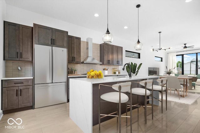 1100 English Ave, Indianapolis, IN 46203 - kitchen featuring freestanding refrigerator, wall chimney exhaust hood, tasteful backsplash, light countertops, and light wood-style floors