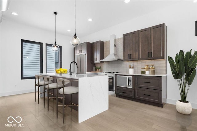 1100 English Ave, Indianapolis, IN 46203 - kitchen featuring wall chimney range hood, white range with gas cooktop, stainless steel refrigerator, dark brown cabinets, and a kitchen island with sink