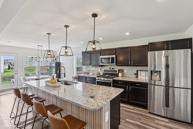1414 W Springhurst Blvd, Greenfield, IN 46140 - kitchen with appliances with stainless steel finishes, light wood-type flooring, a kitchen breakfast bar, tasteful backsplash, and a center island with sink