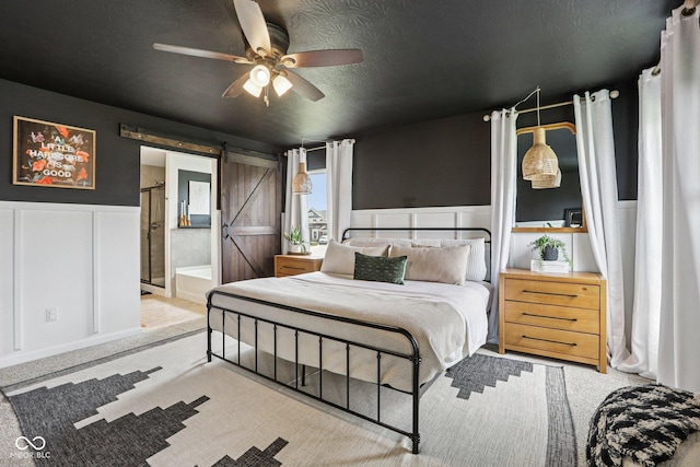 1414 W Springhurst Blvd, Greenfield, IN 46140 - bedroom featuring a barn door, wainscoting, a decorative wall, ceiling fan, and ensuite bathroom