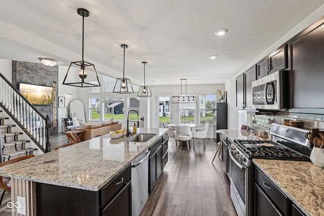 1414 W Springhurst Blvd, Greenfield, IN 46140 - kitchen with stainless steel appliances, dark wood-style floors, light stone counters, decorative light fixtures, and a center island with sink
