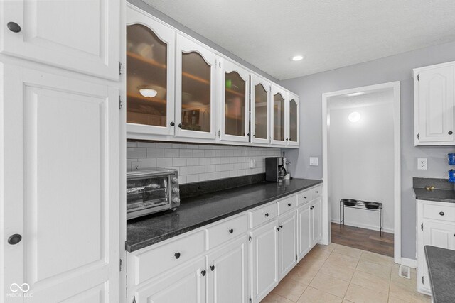 401 N Nicole Ln, Scottsburg, IN 47170 - kitchen with dark countertops, backsplash, white cabinets, glass insert cabinets, and light tile patterned floors