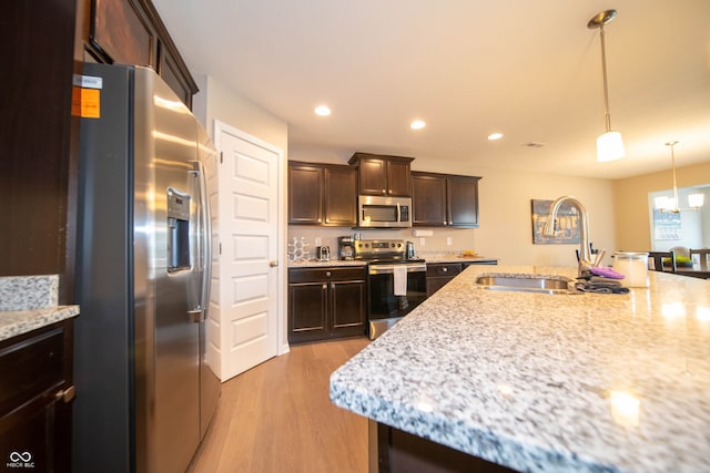 610 Sawtooth St, Westfield, IN 46074 - kitchen featuring appliances with stainless steel finishes, dark brown cabinetry, light wood-style flooring, decorative light fixtures, and light stone countertops