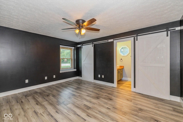 12661 Doe Ln, Indianapolis, IN 46236 - unfurnished bedroom with a barn door, a textured ceiling, wood finished floors, connected bathroom, and a ceiling fan