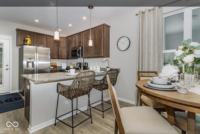 3933 Wren Dr, Brownsburg, IN 46112 - kitchen featuring stainless steel appliances, light wood-type flooring, light stone countertops, dark brown cabinetry, and decorative light fixtures