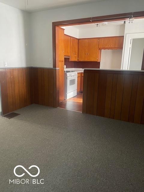 416 W 21st St, Anderson, IN 46016 - kitchen featuring white range with gas stovetop, a wainscoted wall, brown cabinets, and wood walls