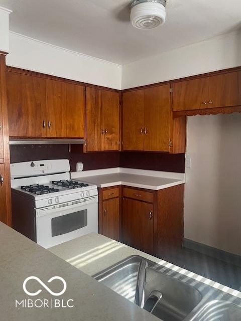416 W 21st St, Anderson, IN 46016 - kitchen with white gas range oven, brown cabinets, light countertops, and exhaust hood