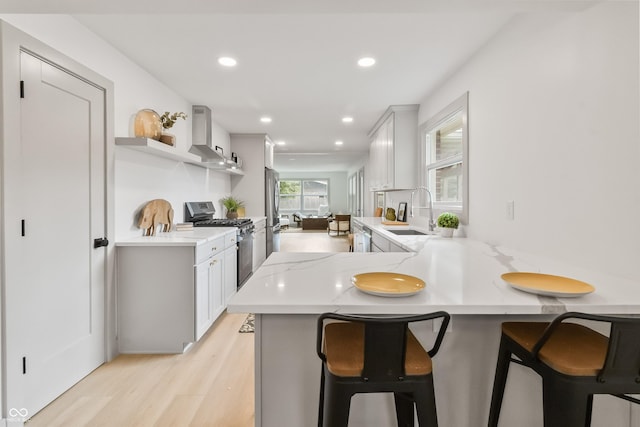 8246 Windcombe Blvd, Indianapolis, IN 46240 - kitchen featuring stainless steel appliances, wall chimney range hood, light wood-style floors, a breakfast bar area, and a peninsula