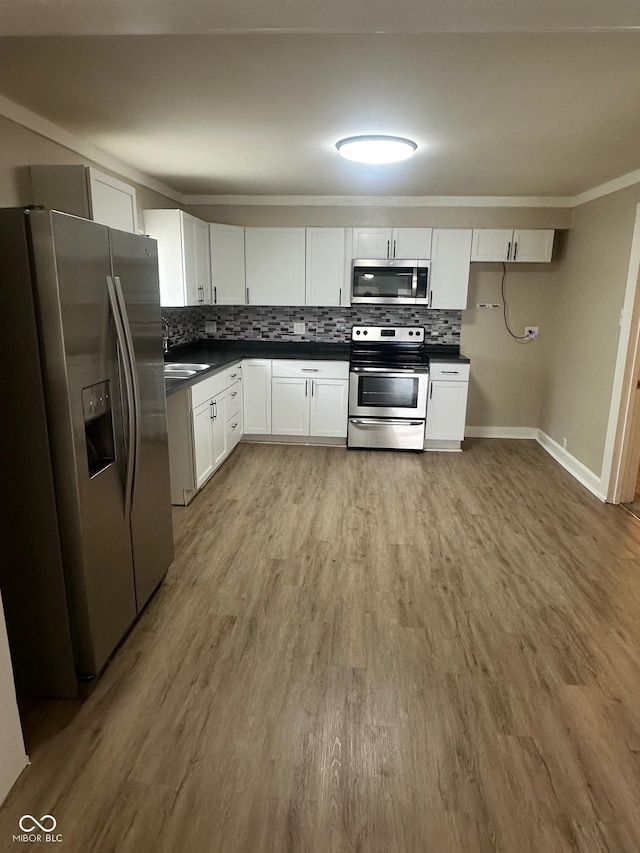 1810 N Parker Ave, Indianapolis, IN 46218 - kitchen with appliances with stainless steel finishes, dark countertops, tasteful backsplash, white cabinetry, and light wood finished floors