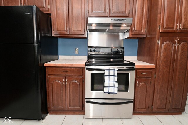 136 W Loretta Dr, Indianapolis, IN 46217 - kitchen featuring freestanding refrigerator, stainless steel electric range oven, under cabinet range hood, tile counters, and light tile patterned floors