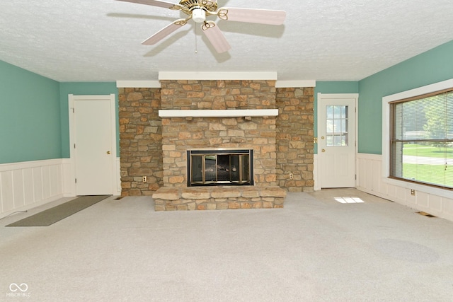 136 W Loretta Dr, Indianapolis, IN 46217 - unfurnished living room featuring a textured ceiling, wainscoting, carpet flooring, a stone fireplace, and ceiling fan