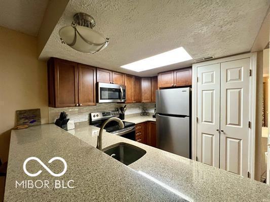 9340 S Lake Ridge Dr Unit 68, Bloomington, IN 47401 - kitchen featuring stainless steel appliances, tasteful backsplash, a textured ceiling, light countertops, and brown cabinetry
