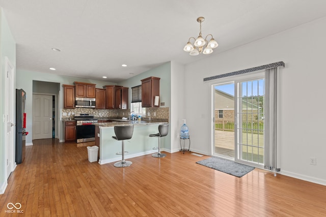 7350 Gold King Way, Indianapolis, IN 46259 - kitchen featuring stainless steel appliances, light wood finished floors, a peninsula, a kitchen breakfast bar, and tasteful backsplash