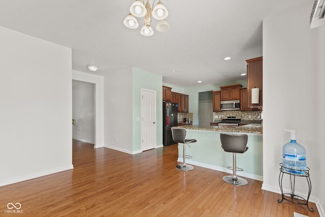 7350 Gold King Way, Indianapolis, IN 46259 - kitchen featuring stainless steel appliances, decorative backsplash, a chandelier, a kitchen breakfast bar, and light wood-style floors