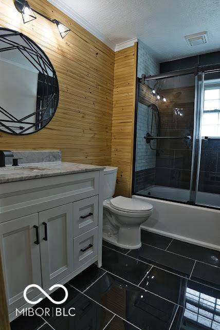 4430 Wexford Rd, Indianapolis, IN 46226 - bathroom with wood walls, vanity, shower / bath combination with glass door, tile patterned floors, and a textured ceiling