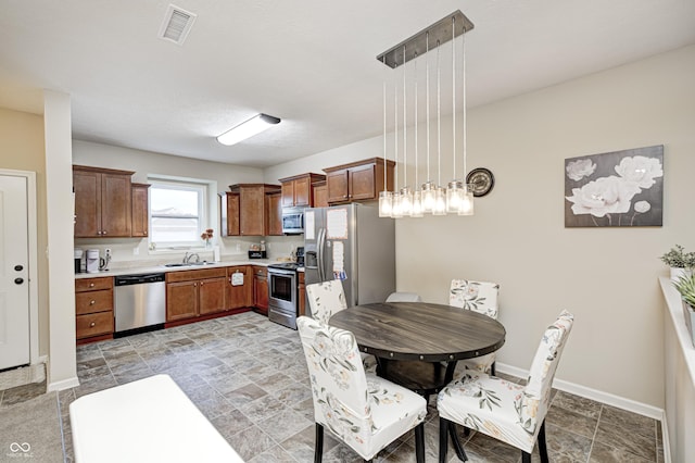 1331 Mccormicks Cir, Danville, IN 46122 - kitchen with stainless steel appliances, light countertops, hanging light fixtures, light stone finish flooring, and brown cabinetry