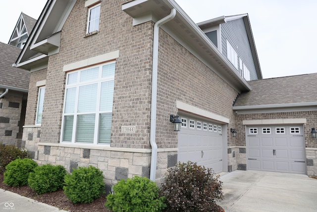 13044 Moorland Ln, Carmel, IN 46074 - view of side of property featuring driveway, stone siding, a garage, and brick siding
