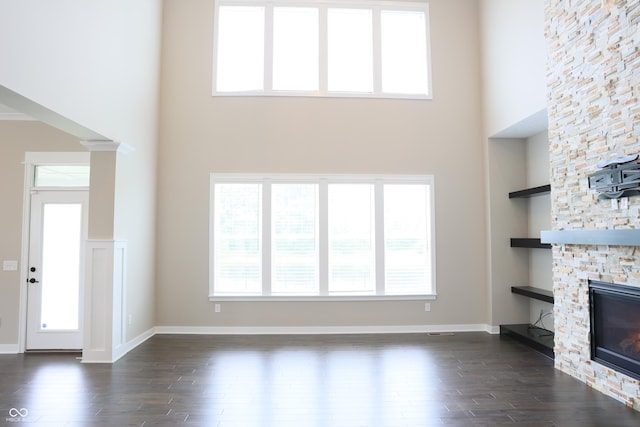 13044 Moorland Ln, Carmel, IN 46074 - unfurnished living room featuring a high ceiling, dark wood-type flooring, built in shelves, a stone fireplace, and healthy amount of natural light