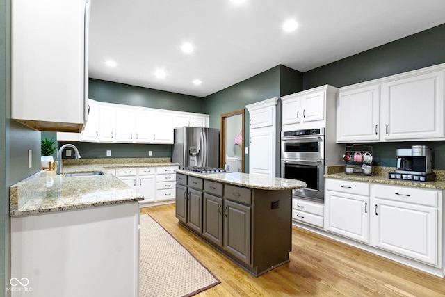 12214 Ridgeside Rd, Indianapolis, IN 46256 - kitchen with appliances with stainless steel finishes, white cabinets, light wood-style flooring, a kitchen island, and light stone counters